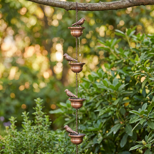 Copper metal bird rain chain wind chime hanging from a tree branch
