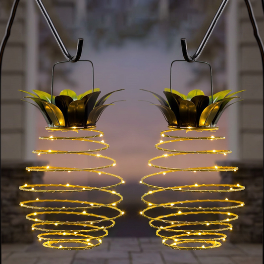 Two solar pineapple lanterns hanging from garden hooks, glowing at dusk